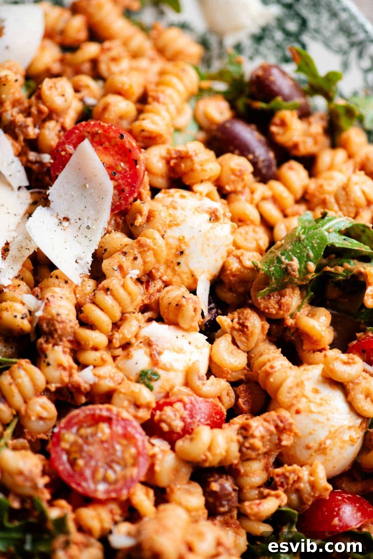 A close up of a pasta salad with a sun-dried tomato sauce, olives, mozzarella and fresh cherry tomatoes.