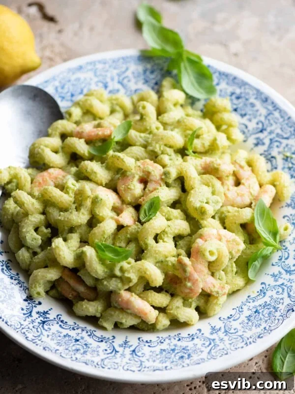 Zucchini shrimp pasta salad in a blue and white bowl topped with basil leaves.