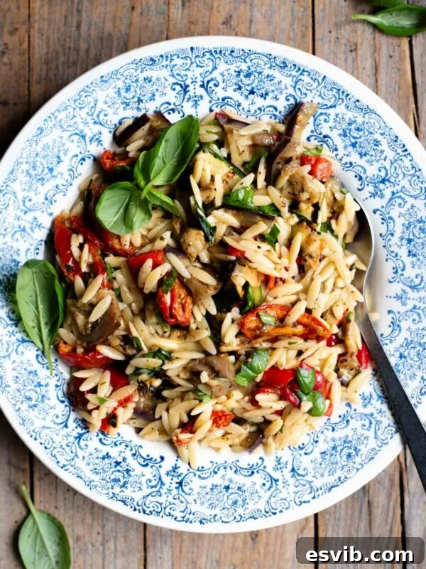 An orzo pasta salad with grilled veg in a blue bowl with a serving spoon at the side. The background is rustic wood.