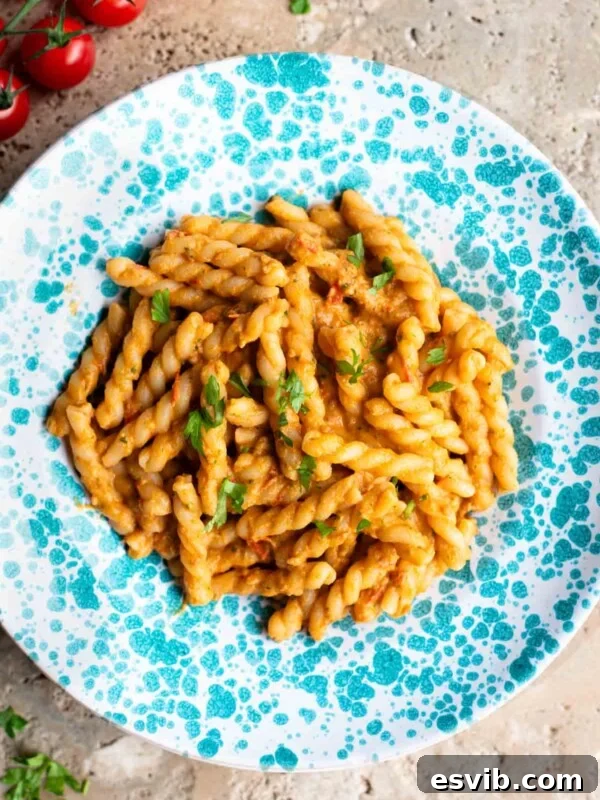 Pasta in a tuna tomato sauce in a blue and white spotted plate sitting on a travertine surface.