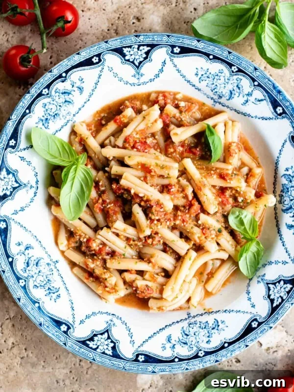 A blue and white vintage bowl with pasta in a fresh tomato sauce topped with basil. The bowl is on a travertine surface with cherry tomatoes and basil around.