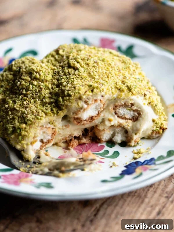 A close up of a piece of pistachio tiramisu on a plate sitting on a wooden table.