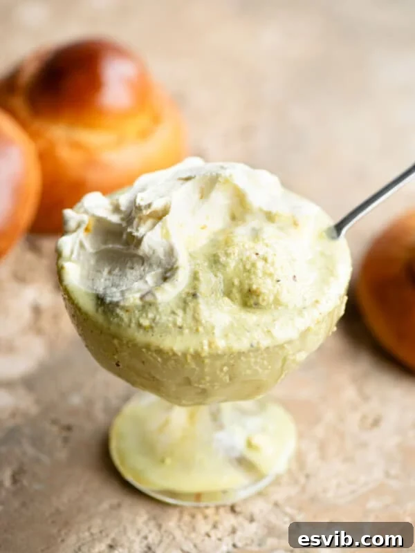 A close up of pistachio granita in a glass serving bowl topped with whipped cream and a brioche bun behind it.