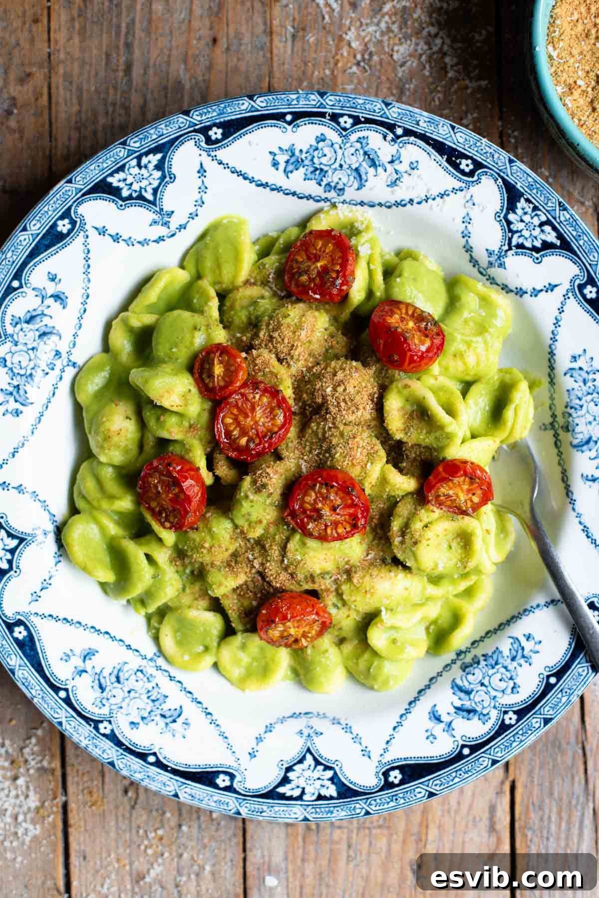 An overhead shot of orecchiette pasta in a vibrant green zucchini sauce with roasted cherry tomatoes on top.