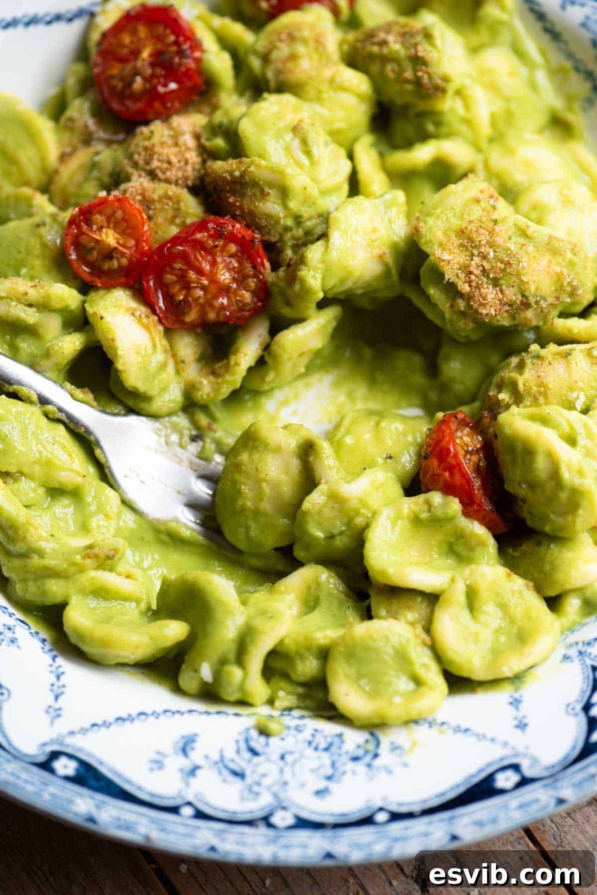 A close up of orecchiette in a smooth vibrant green zucchini sauce with roasted tomatoes on top.