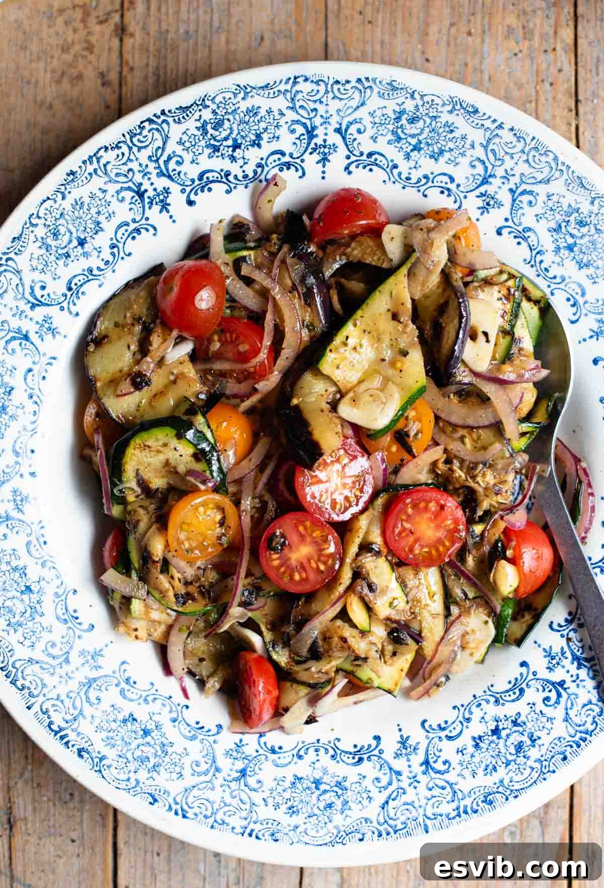 An overhead shot of marinated grilled summer vegetables in a blue bowl on a wooden surface.