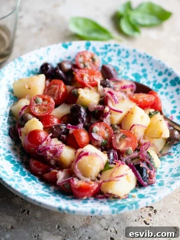 A Sicilian potato salad with olives, tomatoes and onions in a blue and white bowl.