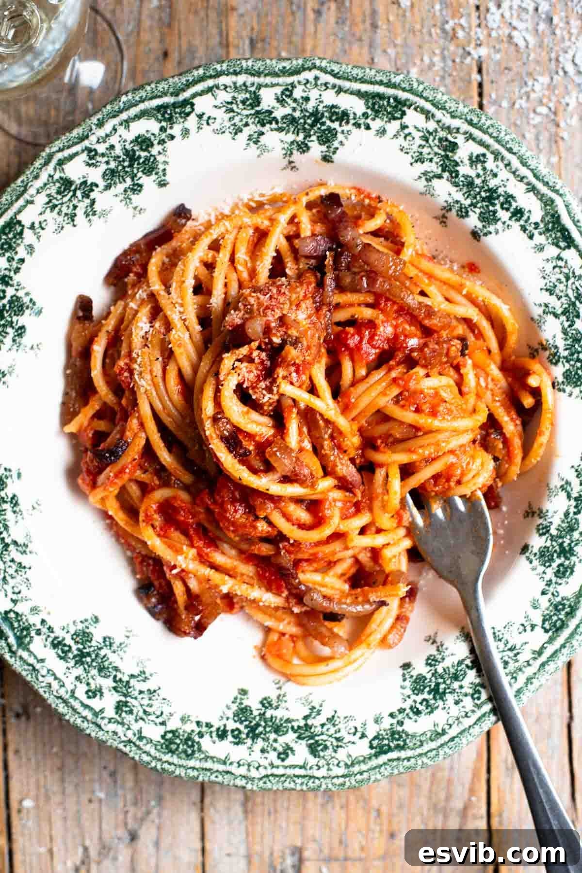 An overhead shot of spaghetti in a green and white vintage style bowl with a tomato and pancetta sauce. The background in rustic wood.