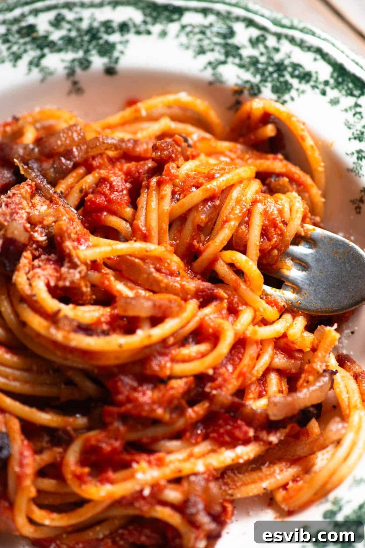A close up of a fork in a bowl with tomato spaghetti topped with pecorino and pancetta.