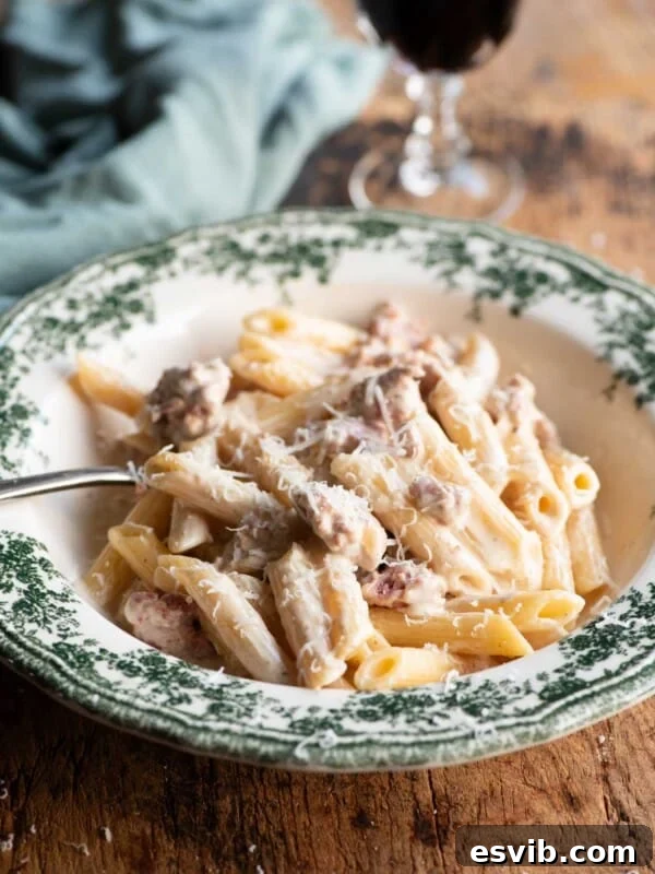 Pasta alla Norcina in a green and white bowl with a fork and glass of wine in the background.