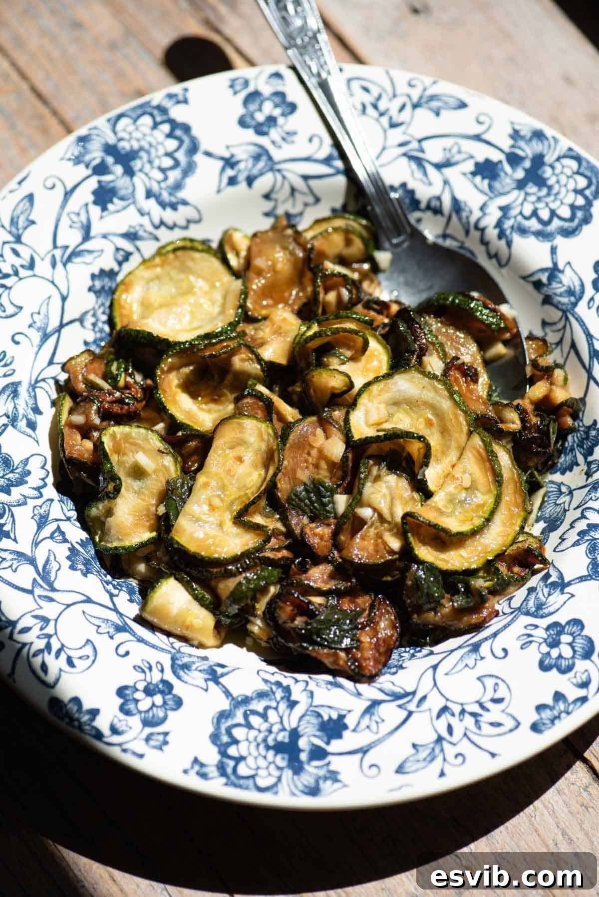 A blue and white floral bowl filled with fried marinated zucchini and a spoon.