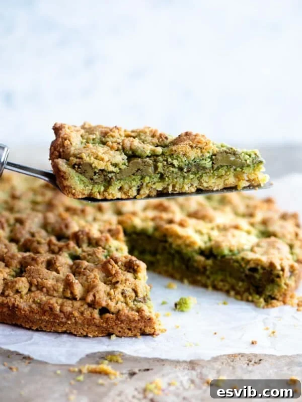 A cake slice holding up a slice of pistachio crumb cake showing a layer of pistachio in the middle.