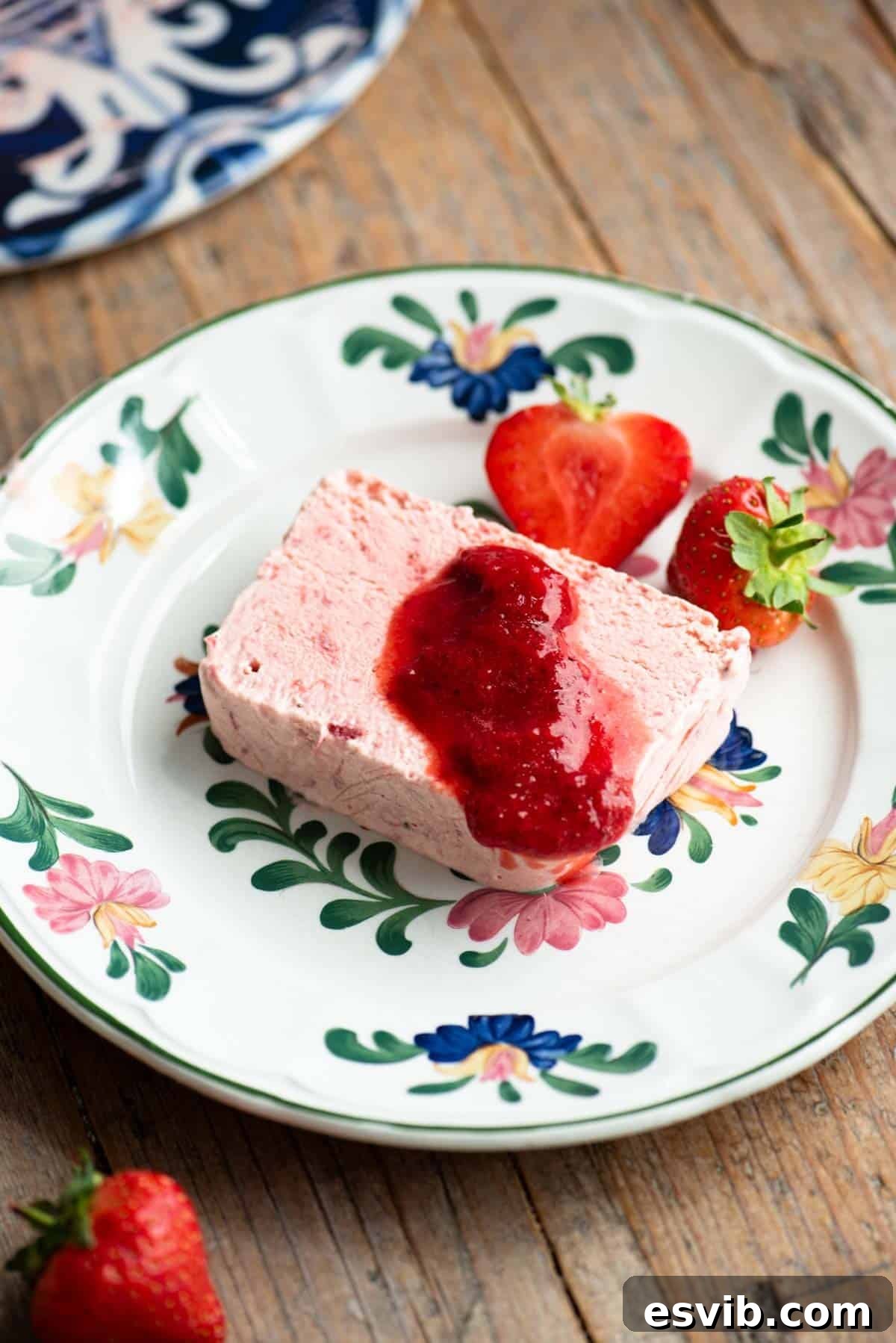 A slice of strawberry semifreddo on a floral plate topped with strawberry sauce.