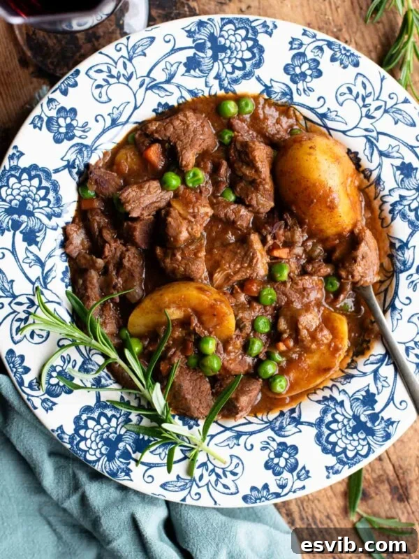 Italian beef stew with potatoes and peas in a blue and white floral bowl with rosemary and red wine at the side.