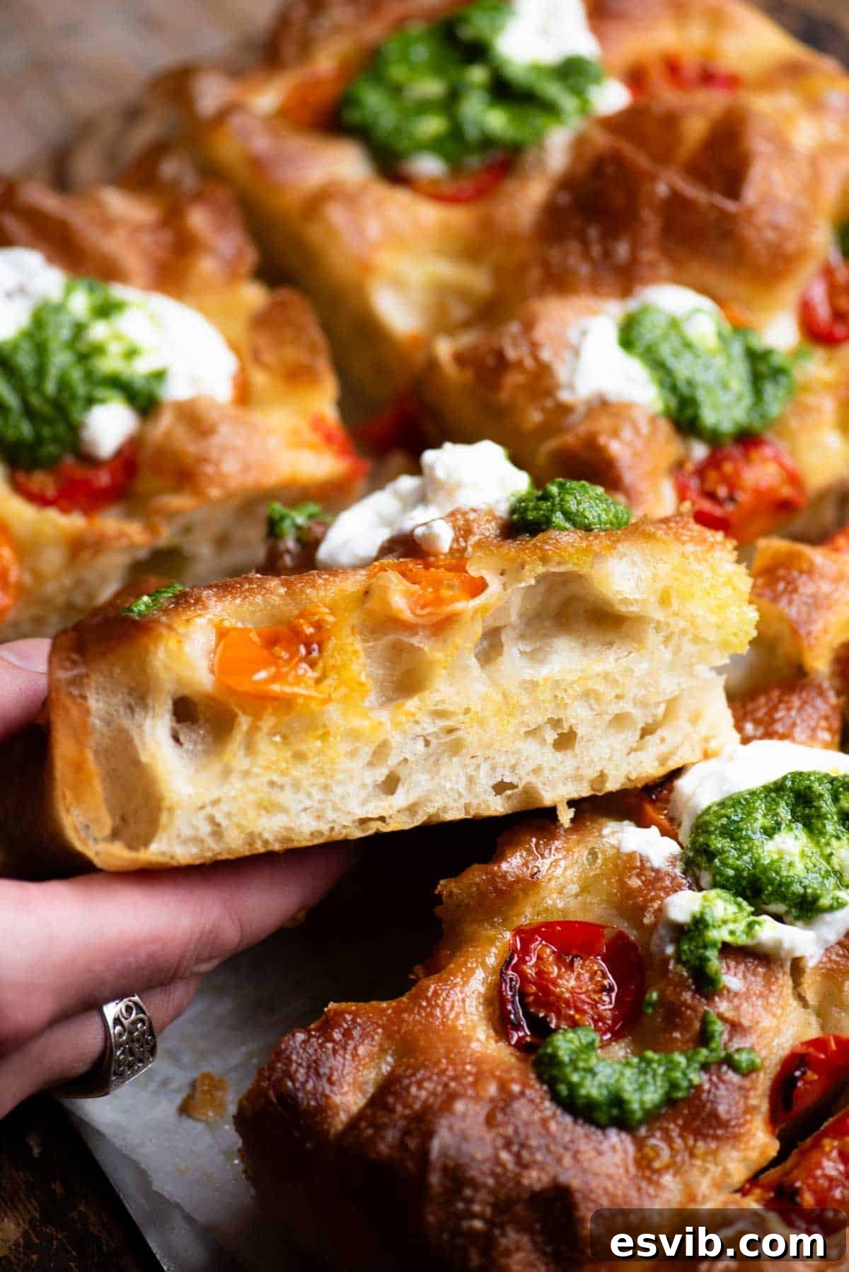 A close up of a hand holding a slice of focaccia showing the airy and light texture inside.