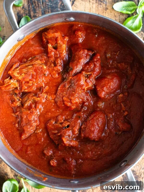 An overhead shot of Sugo Napoletano (Neapolitan ragu) in a large pot sitting on a wooden surface.