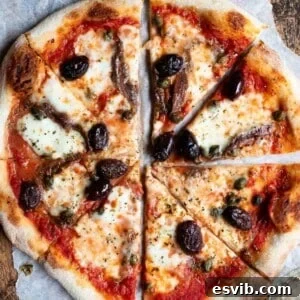 A close up of a pizza cut into slices topped with olives, capers ad anchovies.