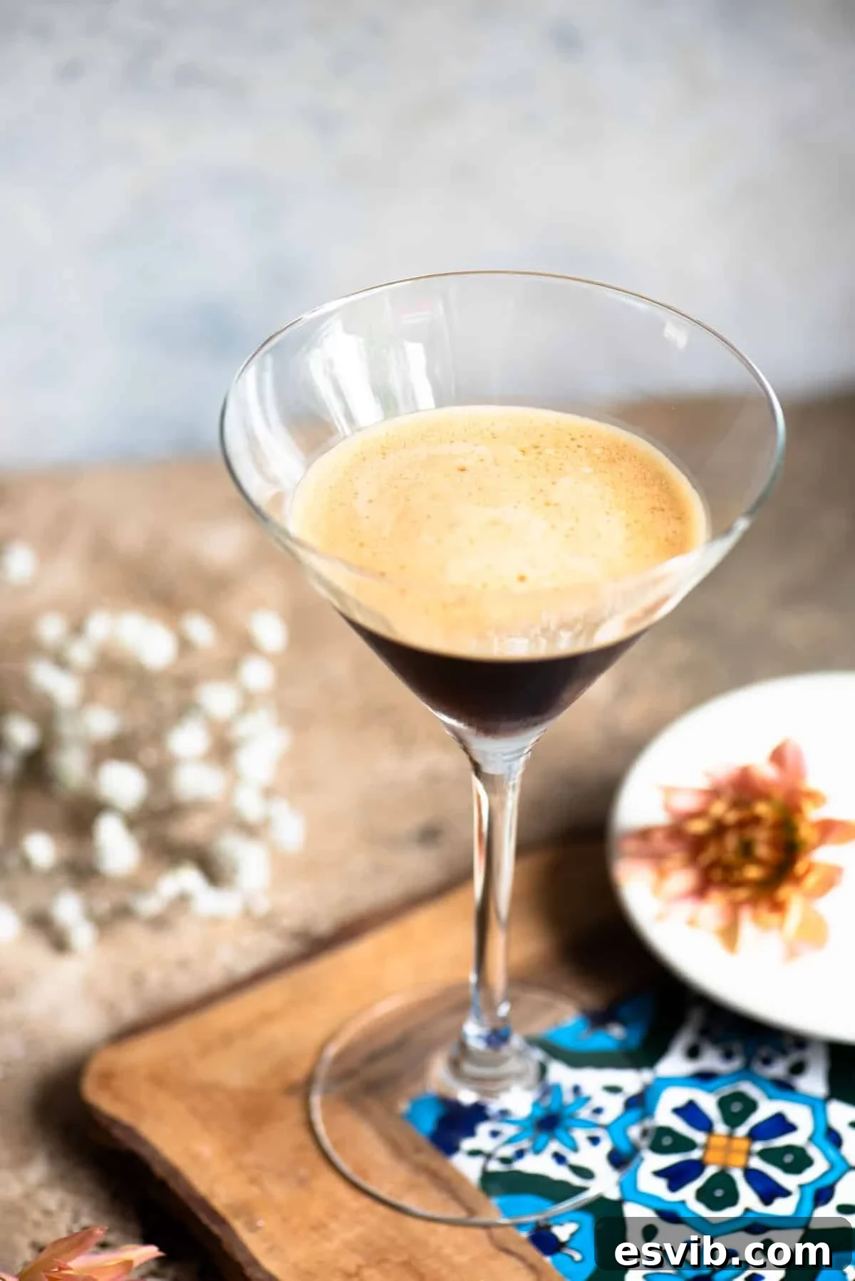 Caffe Shakerato: Classic Italian Iced Coffee Recipe 3 A martini glass filled with an iced coffee on a patterned tile with flowers at the side.