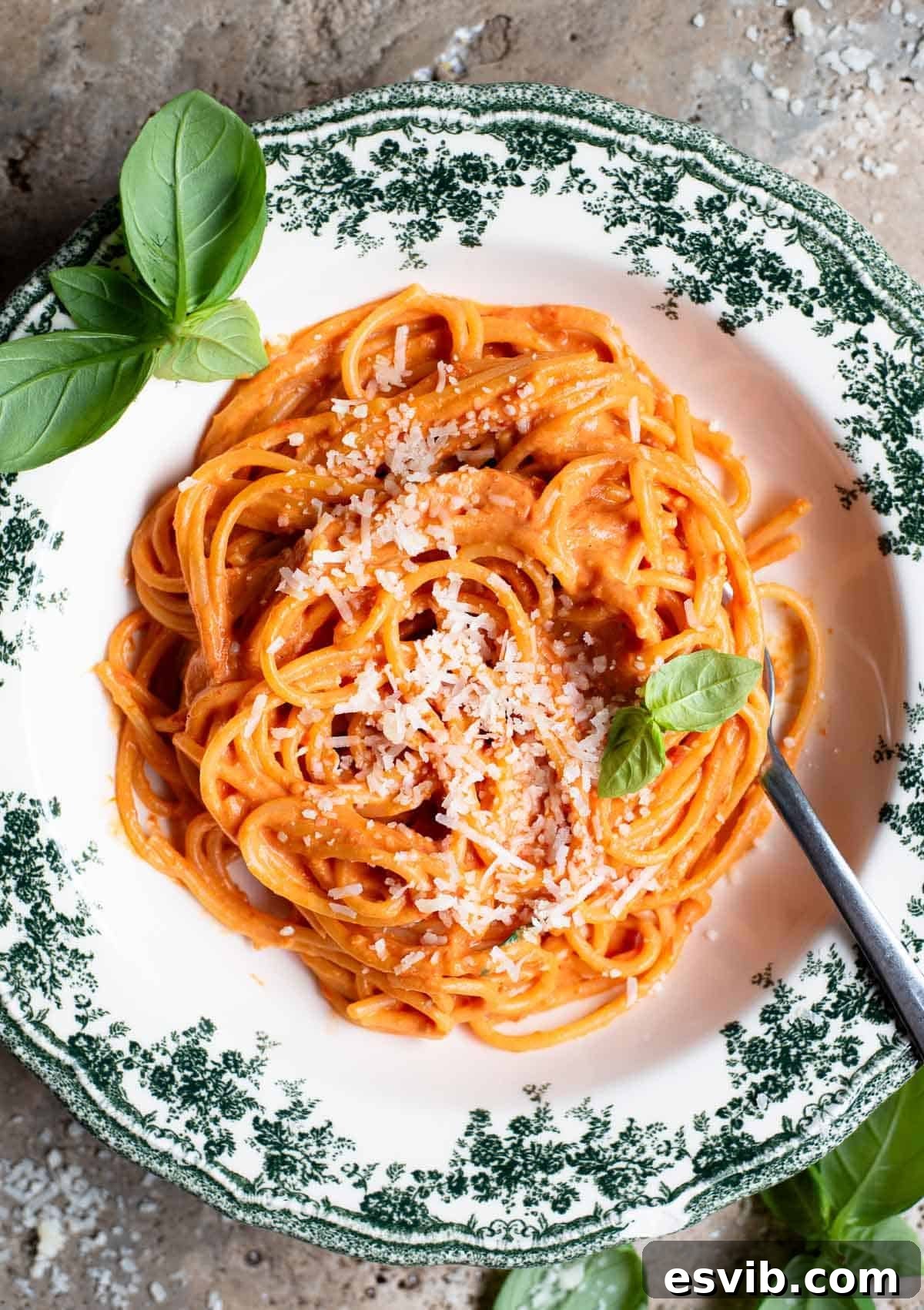 An overhead shot of roasted cherry tomato and ricotta spaghetti in a green floral bowl with basil scattered around.